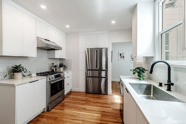 kitchen with a sink, stainless steel appliances, white cabinetry, light wood-type flooring, and under cabinet range hood