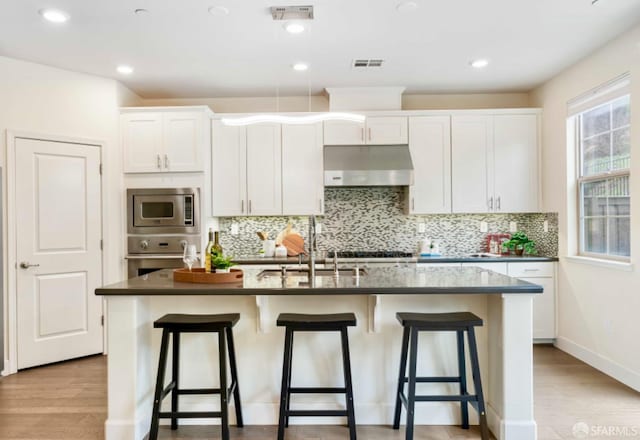 kitchen with stainless steel appliances, sink, an island with sink, white cabinets, and light hardwood / wood-style flooring