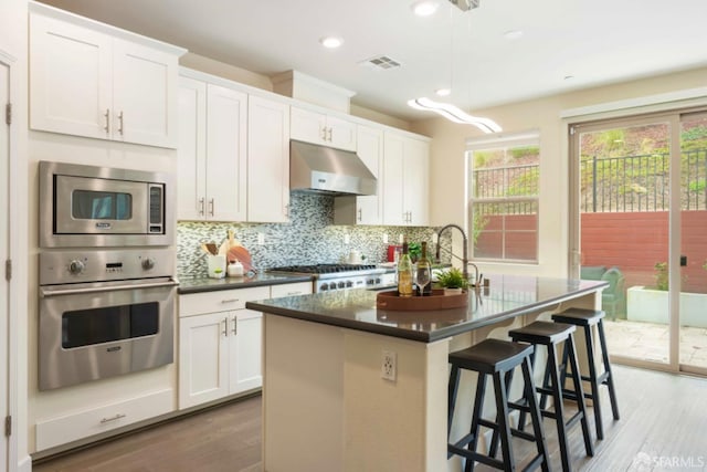 kitchen featuring hardwood / wood-style flooring, white cabinetry, a breakfast bar, appliances with stainless steel finishes, and an island with sink