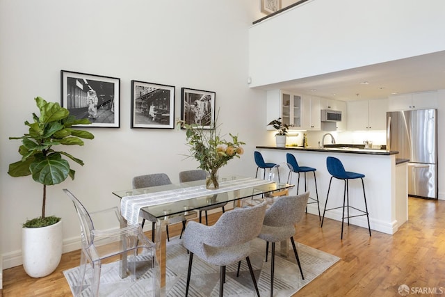 dining room with light wood-type flooring, baseboards, and a high ceiling