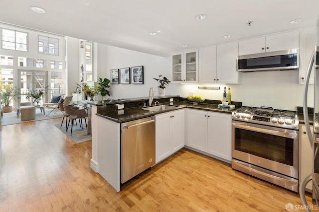 kitchen featuring a sink, white cabinetry, stainless steel appliances, a peninsula, and light wood finished floors