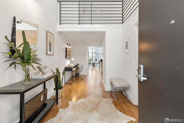 hall with light wood-type flooring, baseboards, and a towering ceiling