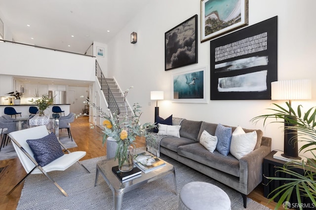 living area with a towering ceiling, recessed lighting, wood finished floors, and stairs