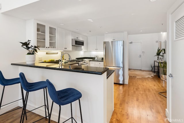 kitchen featuring light wood-style floors, appliances with stainless steel finishes, a peninsula, white cabinets, and glass insert cabinets