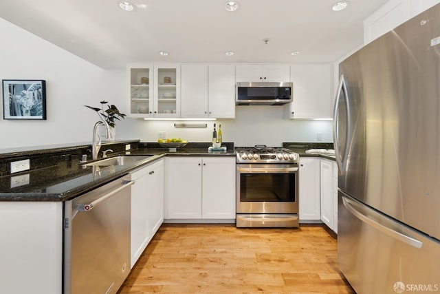 kitchen featuring light wood finished floors, a peninsula, a sink, appliances with stainless steel finishes, and white cabinetry