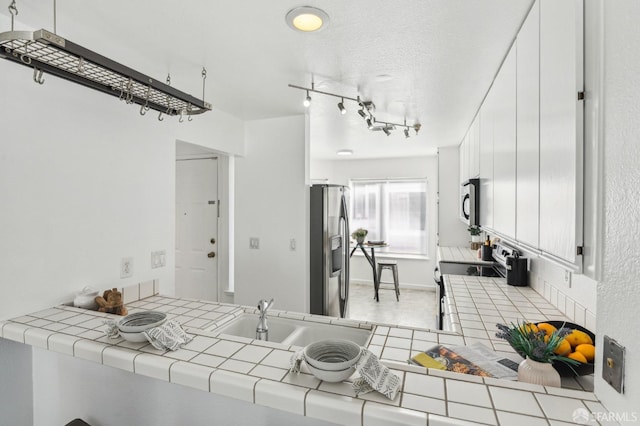 kitchen with stainless steel appliances, a textured ceiling, tile countertops, white cabinets, and sink