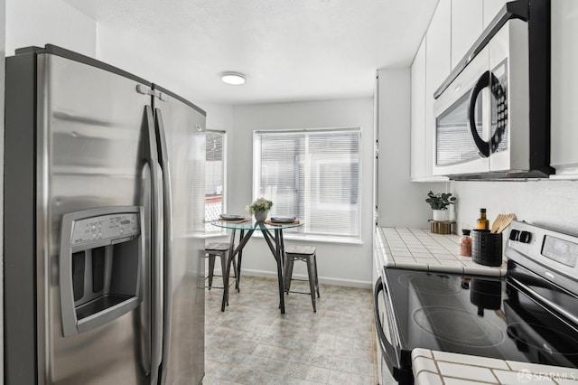 kitchen with appliances with stainless steel finishes, white cabinetry, and tile countertops