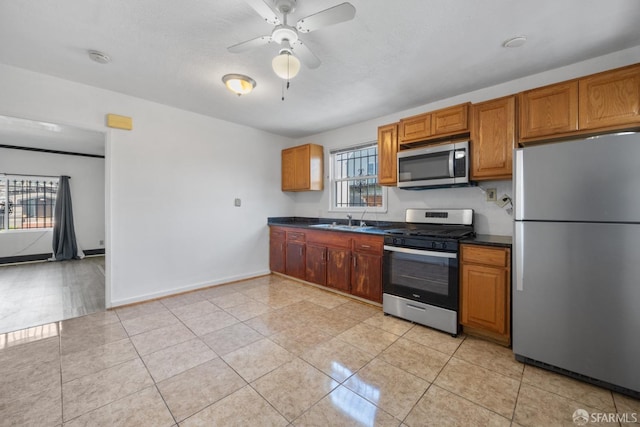 kitchen with a ceiling fan, light tile patterned flooring, dark countertops, stainless steel appliances, and a sink