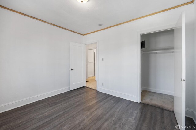 unfurnished bedroom featuring dark wood-type flooring, a closet, baseboards, and ornamental molding
