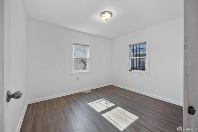 spare room featuring a healthy amount of sunlight, dark wood-style flooring, baseboards, and visible vents