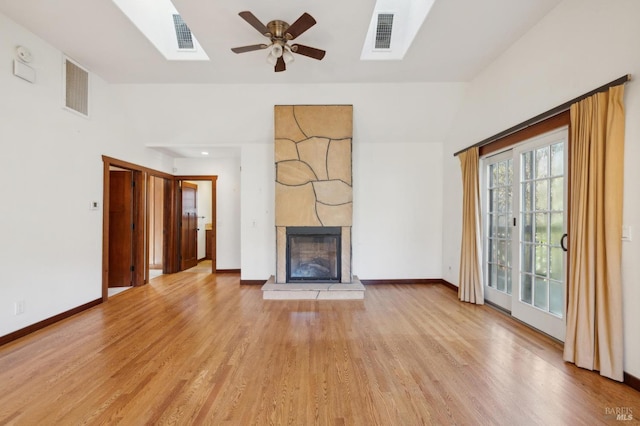 unfurnished living room featuring a skylight, a large fireplace, ceiling fan, and light hardwood / wood-style flooring