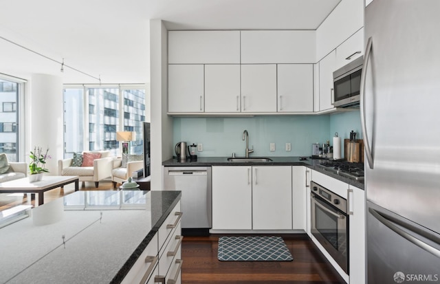 kitchen with white cabinets, dark wood finished floors, dark stone counters, appliances with stainless steel finishes, and a sink