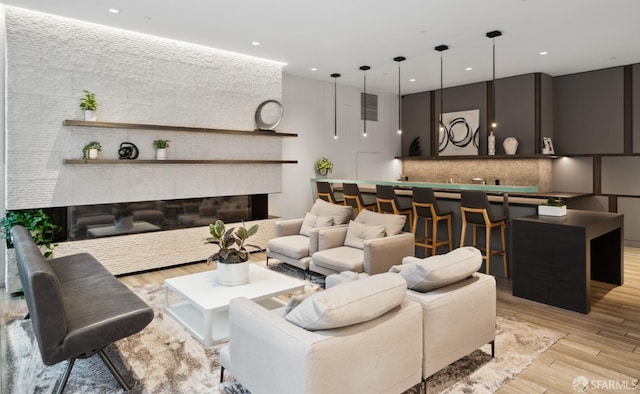 living area featuring wet bar, recessed lighting, a glass covered fireplace, and light wood-style floors