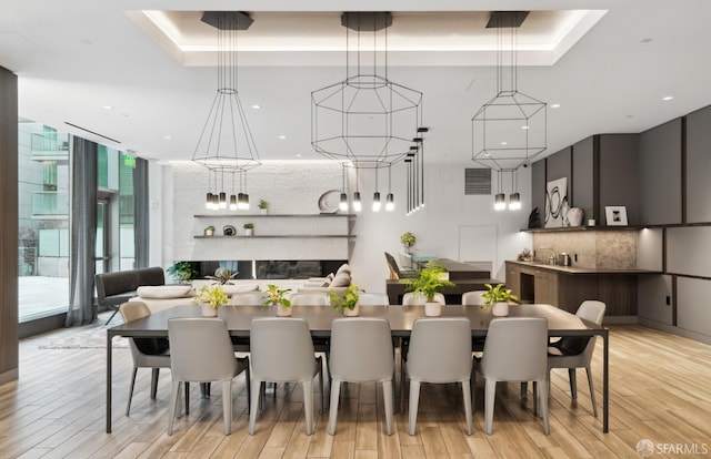 dining area with light wood-style flooring, a tray ceiling, and a wall of windows