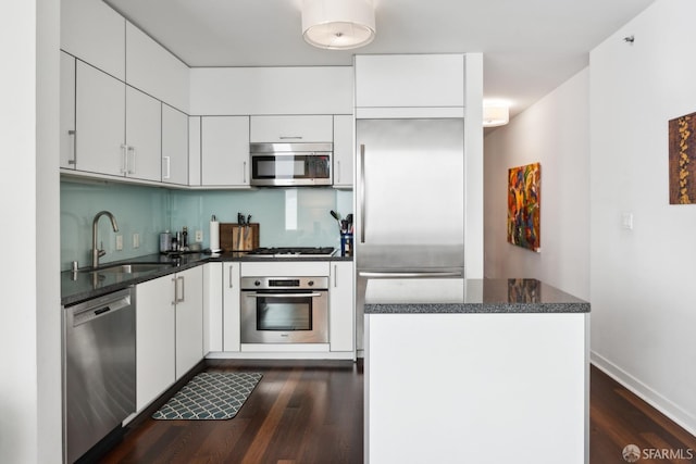 kitchen with white cabinets, dark wood-type flooring, dark stone countertops, stainless steel appliances, and a sink