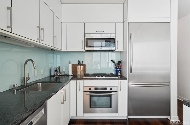 kitchen with appliances with stainless steel finishes, dark stone counters, white cabinetry, and a sink