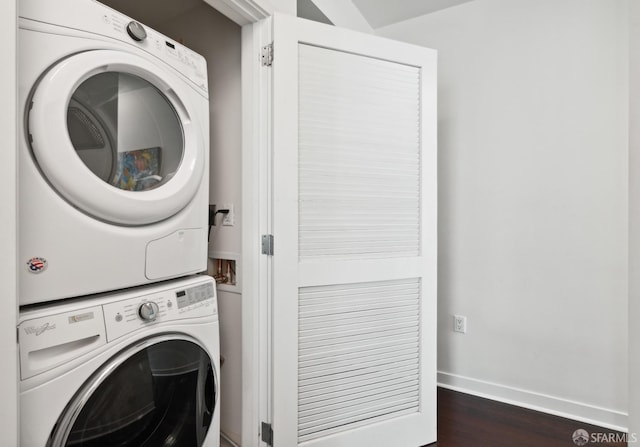 clothes washing area featuring stacked washer and dryer, dark wood finished floors, laundry area, and baseboards