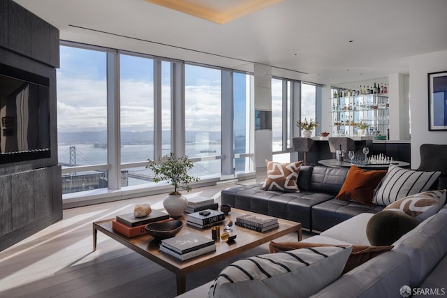 living room with bar area, a wall of windows, light hardwood / wood-style flooring, and a water view