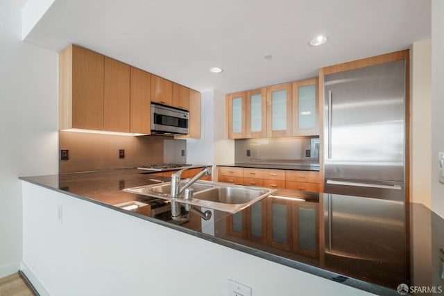 kitchen with a sink, appliances with stainless steel finishes, glass insert cabinets, dark countertops, and recessed lighting