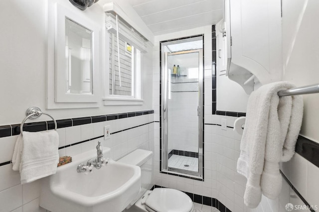 bathroom featuring toilet, sink, tile walls, and a shower with door