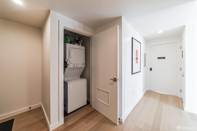 clothes washing area featuring stacked washing maching and dryer and light hardwood / wood-style floors