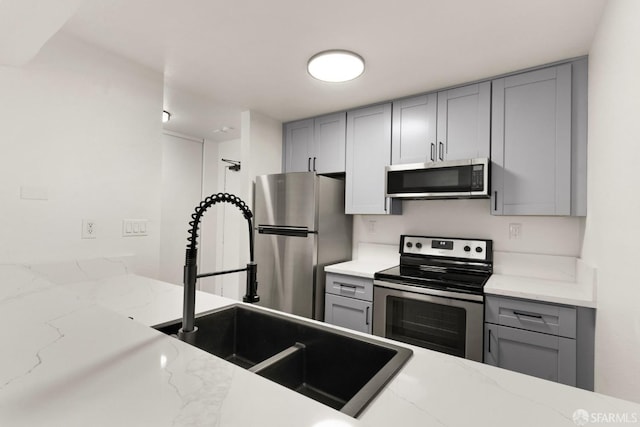 kitchen featuring gray cabinets, light stone countertops, and appliances with stainless steel finishes