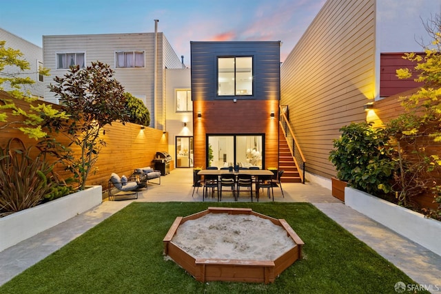 back of house at dusk featuring a lawn, a patio area, fence, and a jacuzzi