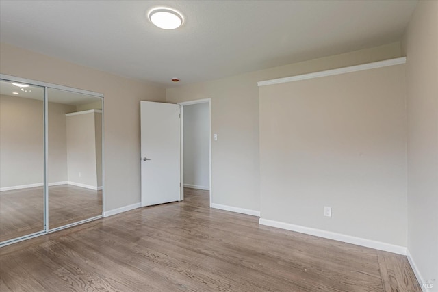 unfurnished bedroom with a closet, wood finished floors, and baseboards