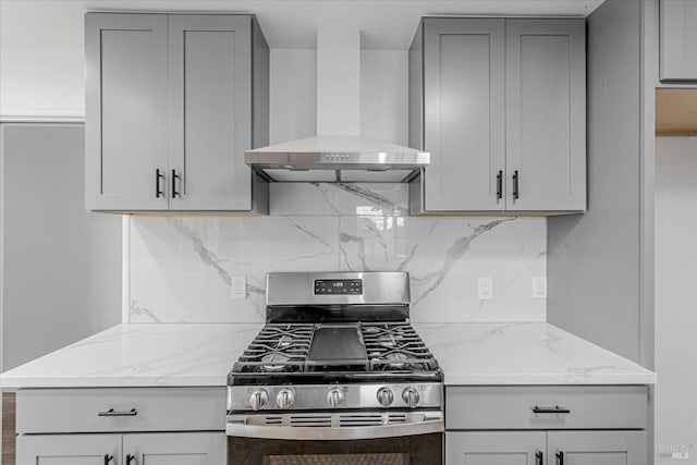 kitchen featuring wall chimney exhaust hood, light stone counters, stainless steel range with gas stovetop, and gray cabinetry