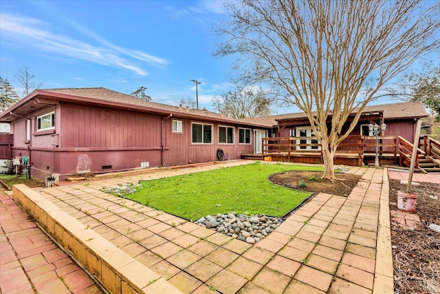 rear view of house with a deck, roof with shingles, crawl space, and a lawn