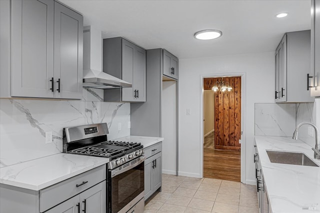 kitchen featuring stainless steel gas stove, light stone counters, gray cabinetry, wall chimney range hood, and a sink