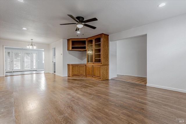 unfurnished living room featuring recessed lighting, baseboards, wood finished floors, and ceiling fan with notable chandelier