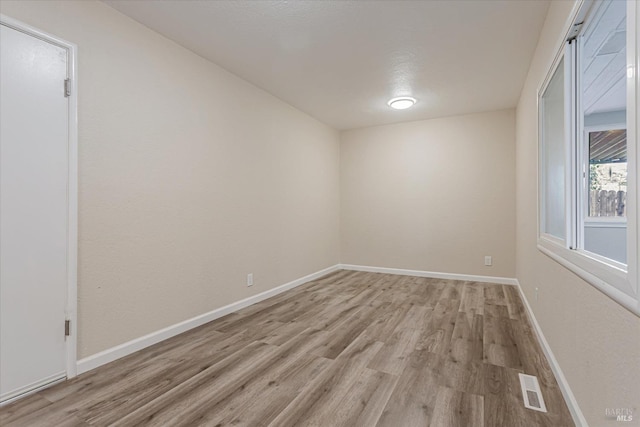 unfurnished room featuring light wood-style floors, visible vents, and baseboards