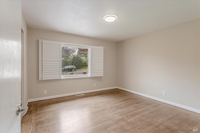 empty room featuring a textured ceiling, wood finished floors, and baseboards