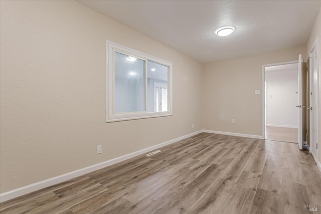 unfurnished room with light wood-type flooring, visible vents, and baseboards