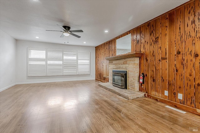 unfurnished living room with a fireplace, a ceiling fan, wood walls, wood finished floors, and baseboards