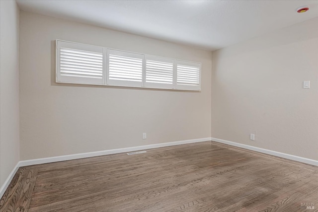 spare room with baseboards and wood finished floors