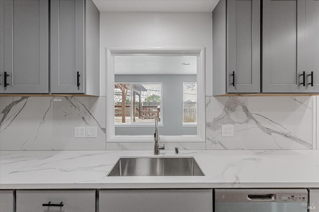 kitchen featuring dishwasher, a sink, gray cabinets, and decorative backsplash