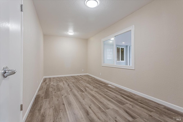 spare room featuring a textured ceiling, light wood finished floors, and baseboards