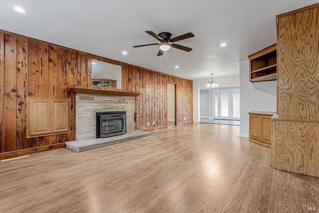 unfurnished living room featuring light wood finished floors, ceiling fan with notable chandelier, wood walls, a fireplace, and recessed lighting