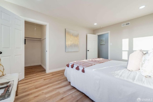 bedroom featuring visible vents, light wood finished floors, attic access, recessed lighting, and a walk in closet