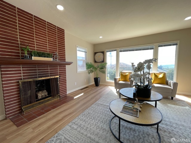 living area featuring visible vents, a brick fireplace, baseboards, and wood finished floors