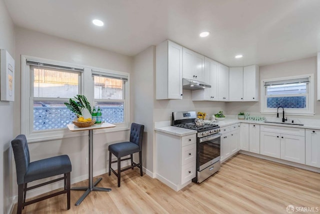 kitchen with light wood-style flooring, a sink, light countertops, under cabinet range hood, and stainless steel gas range oven