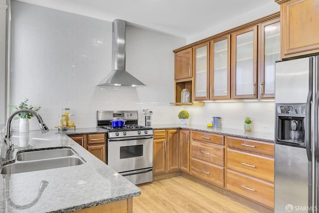 kitchen with light stone countertops, appliances with stainless steel finishes, wall chimney exhaust hood, and sink