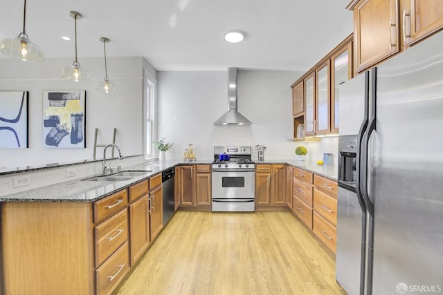 kitchen featuring appliances with stainless steel finishes, dark stone countertops, light hardwood / wood-style floors, decorative light fixtures, and wall chimney range hood