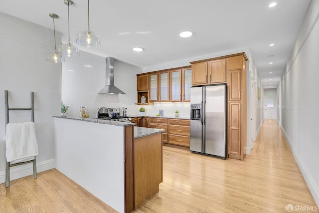 kitchen featuring light hardwood / wood-style floors, kitchen peninsula, stone countertops, stainless steel appliances, and wall chimney range hood