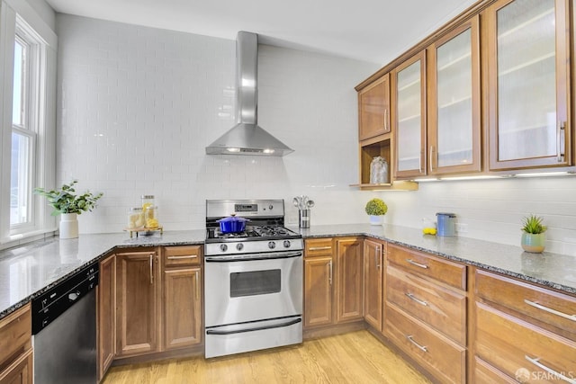 kitchen featuring dark stone counters, appliances with stainless steel finishes, wall chimney range hood, and a healthy amount of sunlight