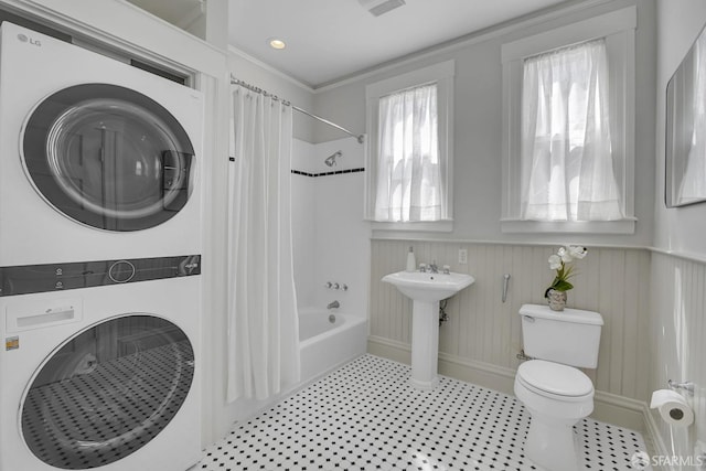 bathroom featuring stacked washer / drying machine, shower / bath combo, crown molding, and toilet