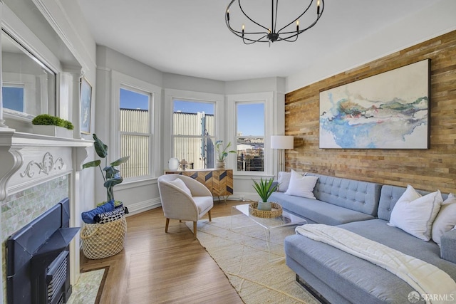 living room with hardwood / wood-style flooring, wooden walls, a tiled fireplace, and a notable chandelier