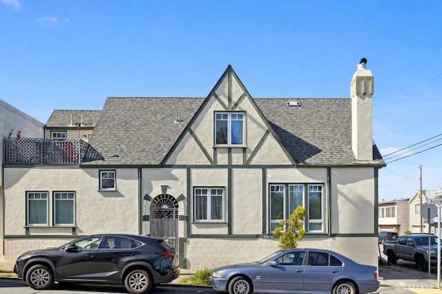 tudor home with stucco siding, a chimney, and a shingled roof